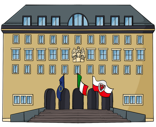 Ein großes gelbes Gebäude. Vor dem Eingang wehen die Fahnen von Europa, Italien und Südtirol.