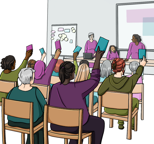 Mehrere Frauen sitzen in Stuhlreihen, mit dem Rücken zum Betrachter. Einige halten farbige Karten in die Höhe. Gegenüber sitzen drei Frauen an einem langen Tisch. Im Hintergrund sind eine Leinwand und eine Flipchart.