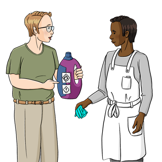 Eine Frau hält eine Plastikflasche mit Gefahrensymbolen in der Hand. Sie zeigt darauf und redet. Neben ihr stehen ein Mann in weißer Schürze. Er hält Handschuhe in der Hand.