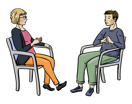 Eine Beraterin und ein Mann sitzen sich in Sesseln gegenüber. Zwischen ihnen steht ein kleiner Tisch mit Info-Heften.
