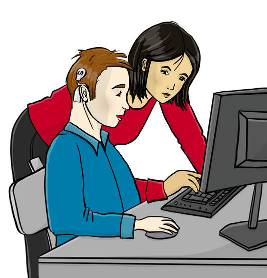 Ein Mann mit einem Cochlea-Implantat sitzt am Computer. Neben ihm steht eine Frau und zeigt auf den Bildschirm.