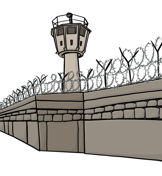 Eine Mauer mit Stacheldraht. Hinter der Mauer steht ein Wachturm.