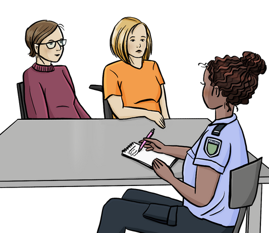 Zwei Frauen sitzen an einem Tisch. Gegenüber sitzt eine Polizistin und schreibt etwas auf. 