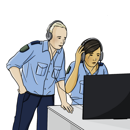 Eine Polizistin sitzt mit Kopfhörern am Computer. Neben ihr steht ein weiterer Polizist mit Kopfhörern. 