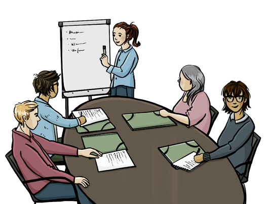 Menschen sitzen um einen Tisch herum. Auf dem Tisch liegen Mappen und Papiere. Eine Frau zeigt auf eine Flipchart.