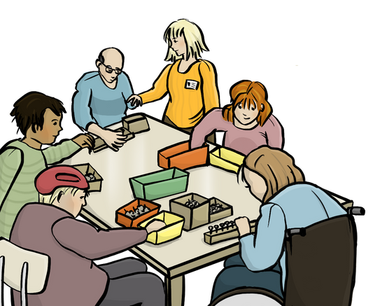 Menschen mit Behinderungen sitzen um einen Tisch herum und legen Dinge in Schachteln. Eine Frau mit einem Namensschild hat einem Mann die Hand auf die Schulter gelegt.