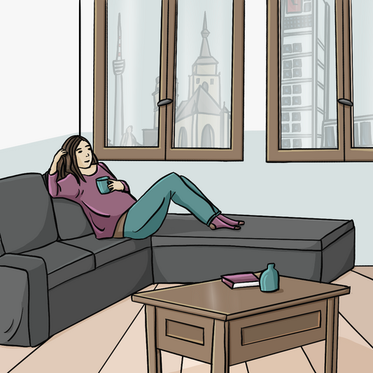 Eine Frau sitzt in einem Wohnzimmer auf einem Sofa mit einer Tasse in der Hand.